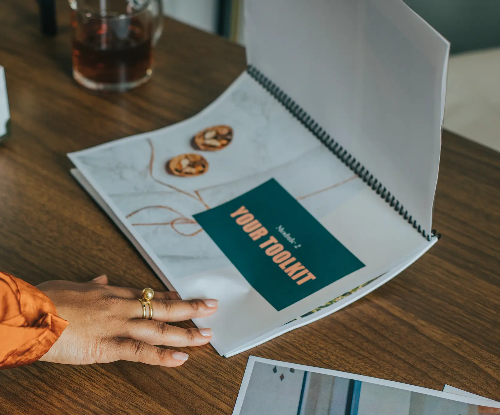 The Creative Flow Audit workbook open on a desk showing Module 2: Your Toolkit, Rachel's hand resting on the page